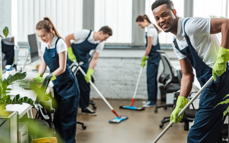 selective focus of smiling multicultural team of cleaners washing floor with mops in office selective focus of smiling multicultural team of cleaners washing floor with mops in office